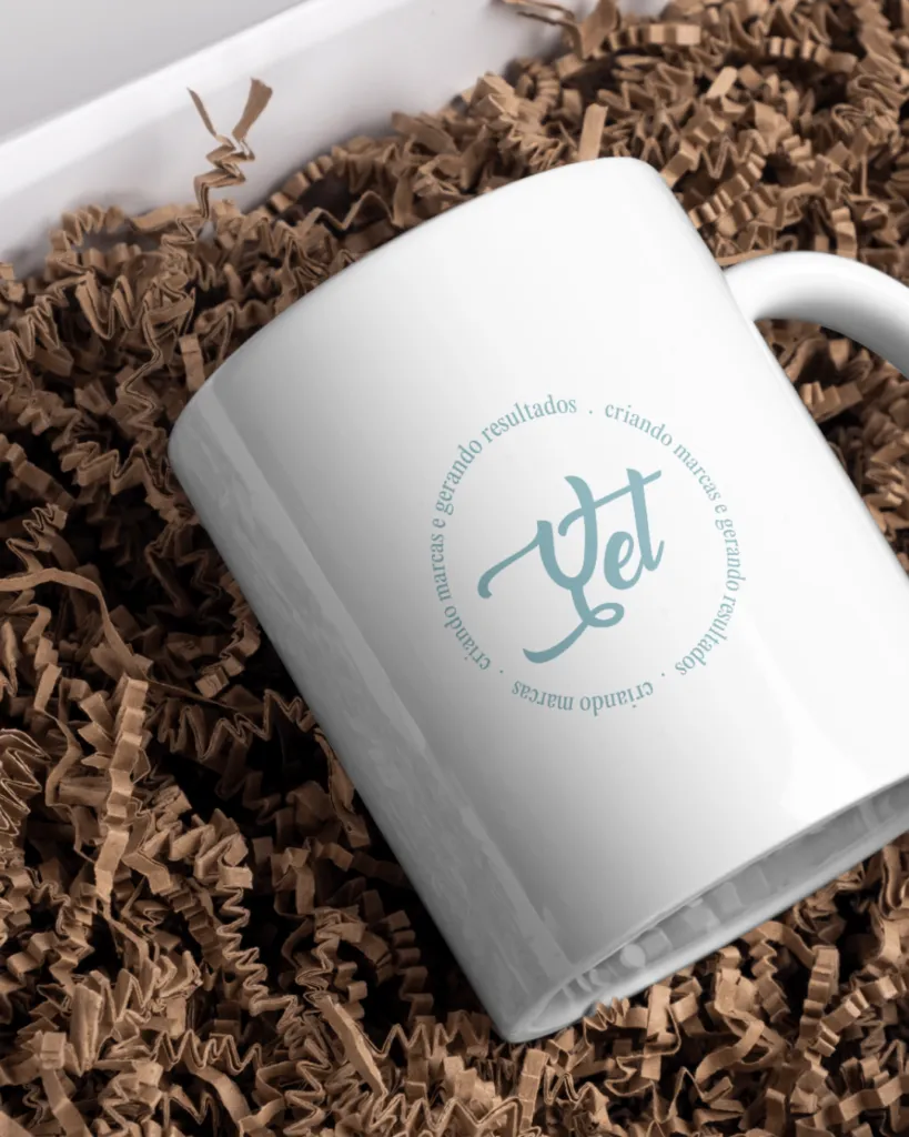 Caneca com a identidade visual da Yet Agência sobre papel kraft
